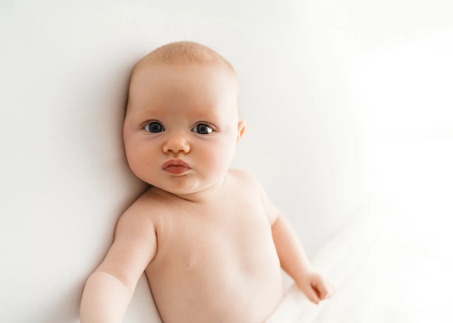 Baby with big blue eyes looking up at camera on white background - baby photographer Kingston