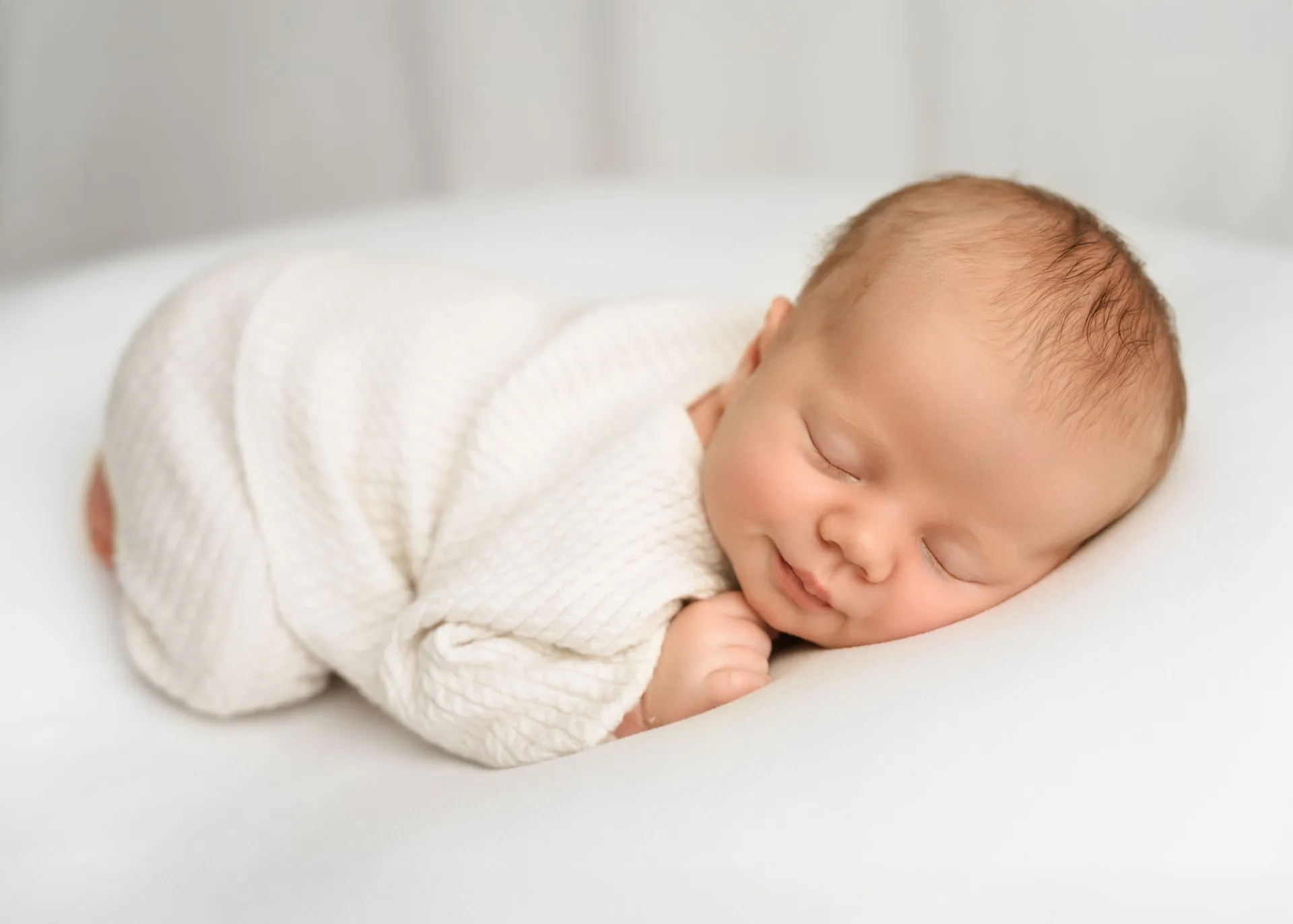 Peaceful newborn in cream knit outfit sleeping on white surface